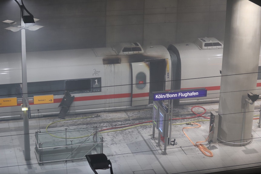 Das Foto zeigt einen ICE von außen mit starken Brandspuren an den Türen. Der Zug steht im verrauchten Flughafen-Bahnhof