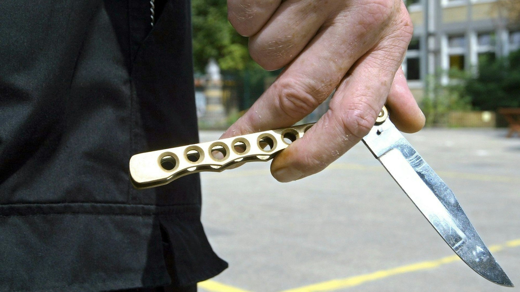 Eine Person hält auf dem Hof einer Schule ein so genanntes Butterflymesser in seiner Hand.