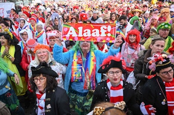 Feiernde am Heumarkt Köln. Eine verkleidete Frau hält ein Schild mit der Aufschrift „Alaaf!“ in die Luft.