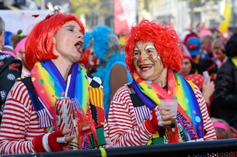 Zwei Frauen tragen rote Perücken und stehen an einer Absperrung zusammen.