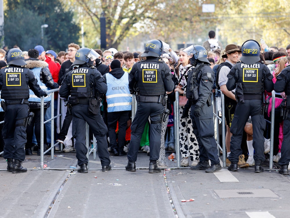 Mehrere Polizisten stehen auf der Zülpicher Straße hinter einer Absperrung und blockieren den Durchgang. Im Hintergrund warten viele junge Besucher.