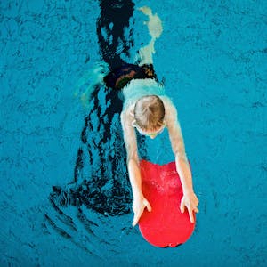Ein Kind, von oben fotografiert, schwimmt mit einer Schwimmhilfe in einem Schwimmbecken.