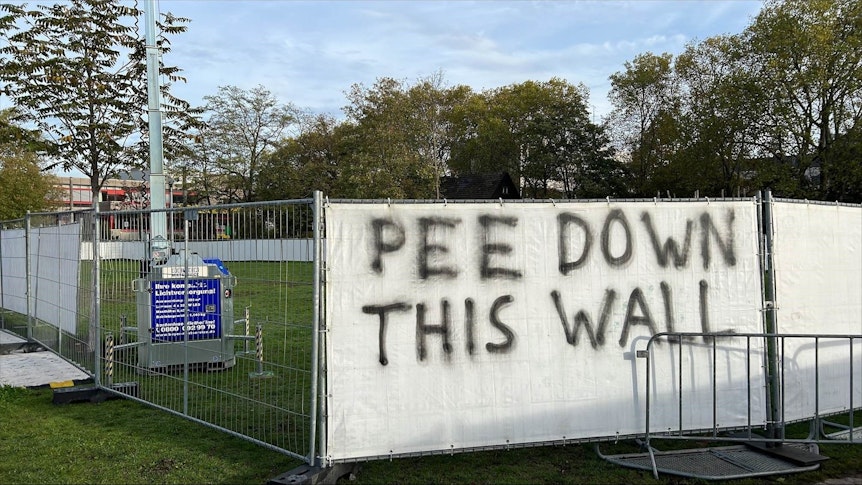 Auf einem Transparent, welches an einem Bauzaun vor den Uniwiesen hängt, steht „Pee Down This Wall“