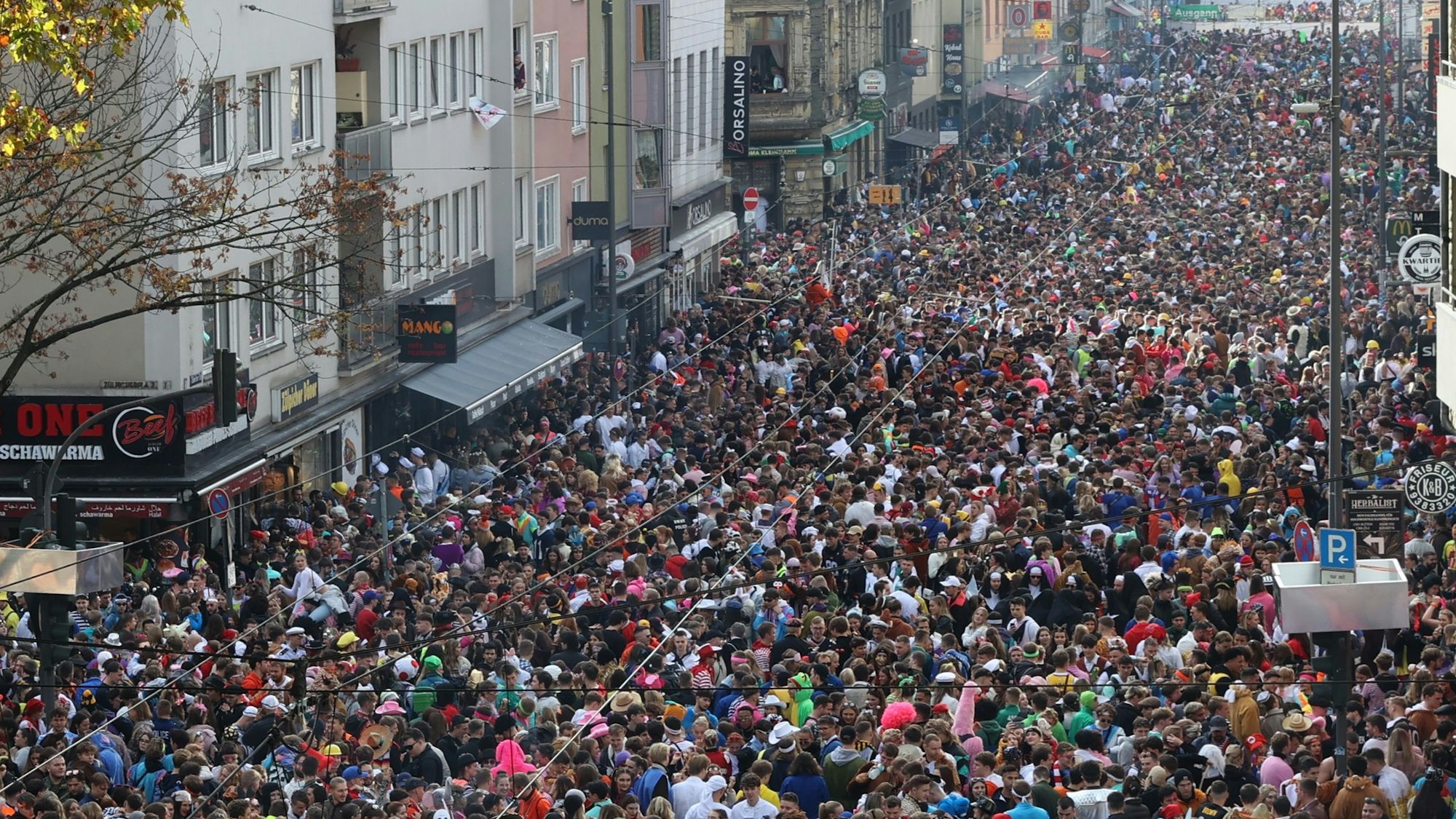 Blick aus einem Fenster auf die Zülpicher Straße, auf der sich Massen kostümierter Menschen drängen, die die gesamte Straßenbreite einnehmen.