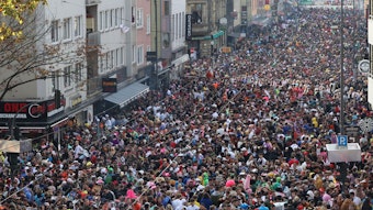 Blick aus einem Fenster auf die Zülpicher Straße, auf der sich Massen kostümierter Menschen drängen, die die gesamte Straßenbreite einnehmen.