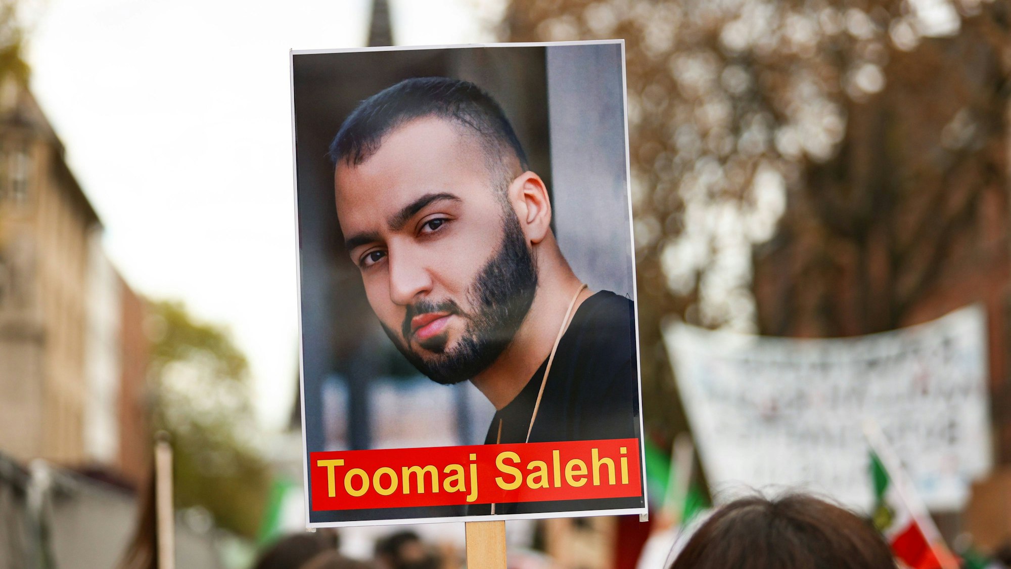 Ein Demonstrierender hält ein Schild mit dem Portrait des iranischen Rapper Toomaj Salehi bei einer Demonstration in Köln in die Höhe.