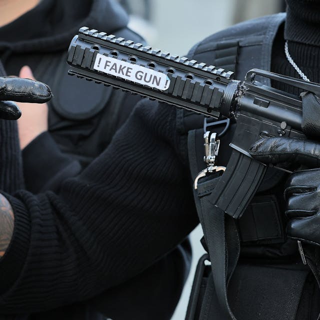 Ein als Swat-Polizist verkleideter Karnevalist hält eine Pistolenattrappe mit der Aufschrift „Fake Gun“ in der Hand.