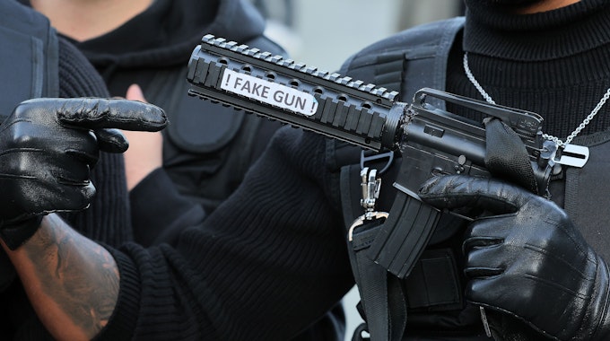 Ein als Swat-Polizist verkleideter Karnevalist hält eine Pistolenattrappe mit der Aufschrift „Fake Gun“ in der Hand.
