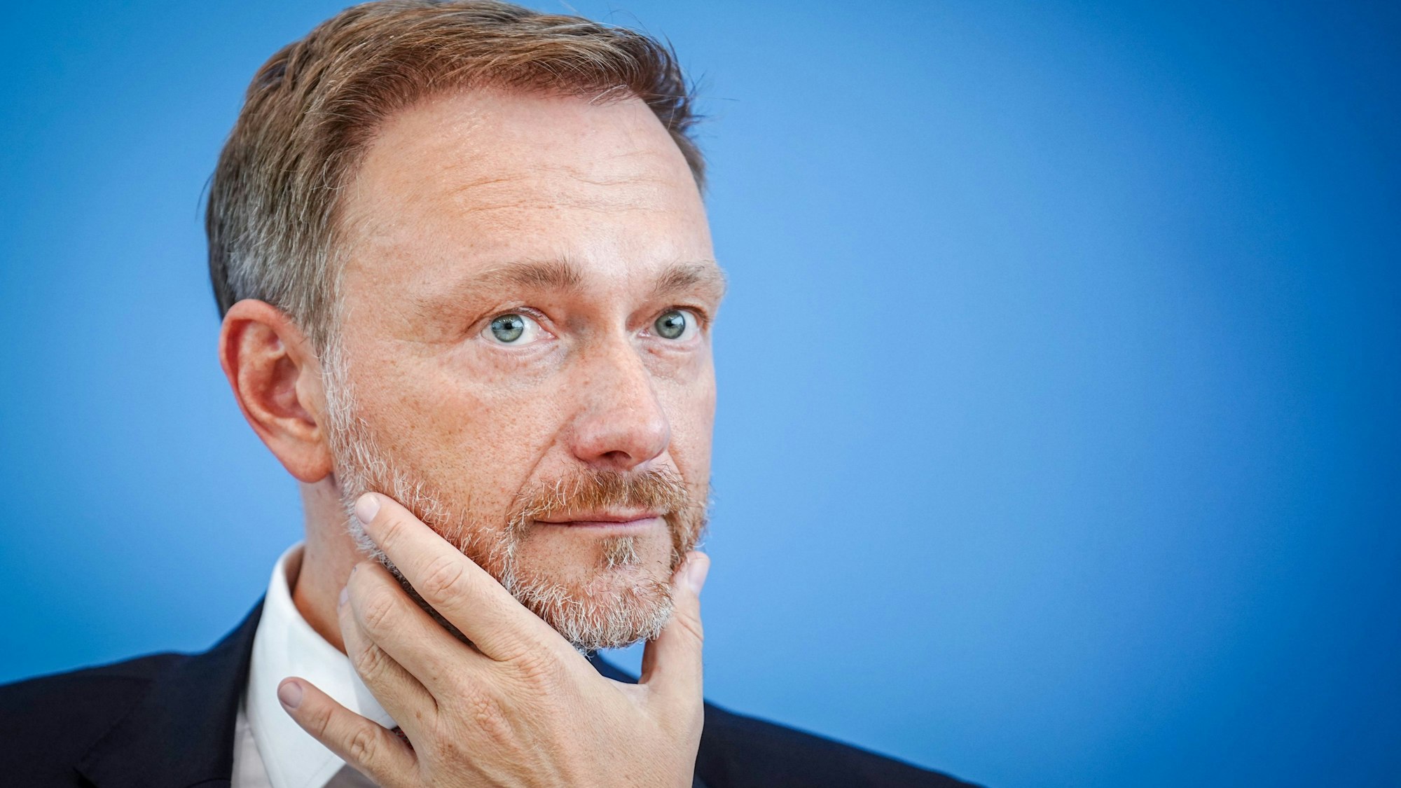 Bundesfinanzminister Christian Lindner in nachdenklicher Pose vor blauem Hintergrund.