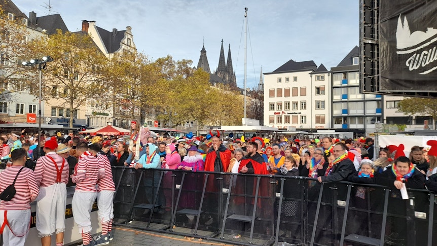 Zahlreiche Karnevalisten stehen vor der Bühne am Heumarkt in Köln. Im Hintergrund sieht man den Dom.