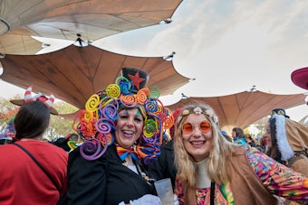 Zwei Frauen stehen im Tanzbrunnen. Eine hat eine Blumenkette im Haar, die andere eine Kopfbedeckung in schrillen Farben.