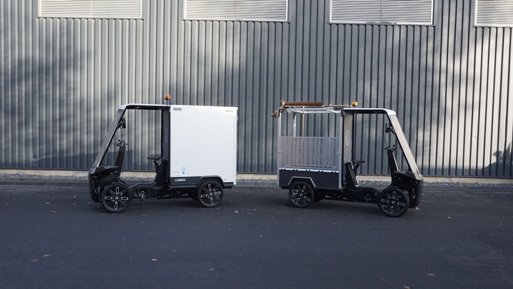 Zwei überdachte Lastenroller stehen vor einem Gebäude.