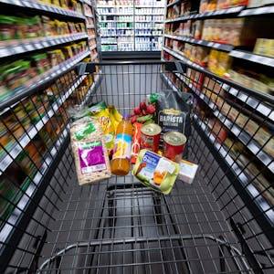Ein Einkaufswagen, gefüllt mit Konserven, Eiern und einigen anderen Lebensmitteln, wird durch einen Gang im Supermarkt geschoben.