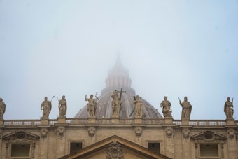 Die Kuppel des Petersdoms in Rom liegt im Nebel. Auf der Bekrönung der Fassade sind Statuen von Christus und den Aposteln zu sehen.
