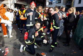Eine Personengruppe trägt Kostüme, die an Feuerwehrkräfte erinnert.