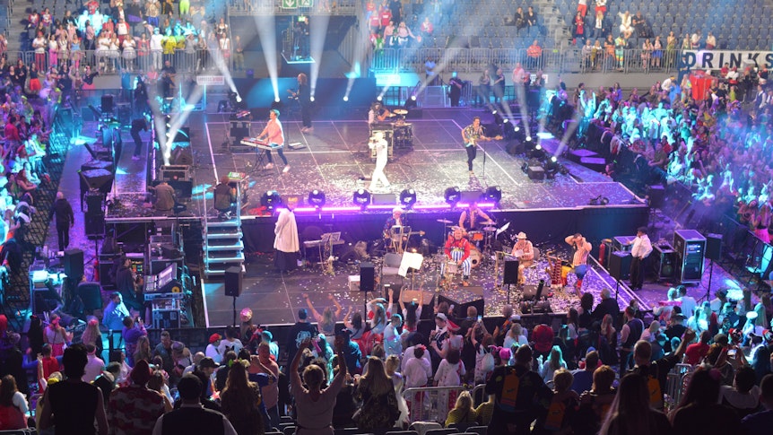 Ein Blick auf die Bühne in der Lanxess-Arena. Musiker stehen auf der Bühne, drumherum feiern die verkleideten Menschen.