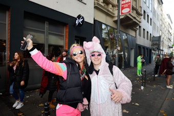 Zwei junge Karnevalisten. Einer trägt ein rosafarbenes Schweinekostüm aus Plüsch.