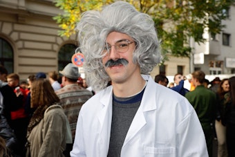 Ein Mann trägt einen weißen Arztkittel mit einer Perücke mit grauem Haar.