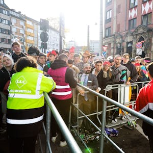 Kostümierte Menschen stehen am 11.11.2022 am Eingang zur Party-Zone auf der Zülpicher Straße vor einer Absperrung.