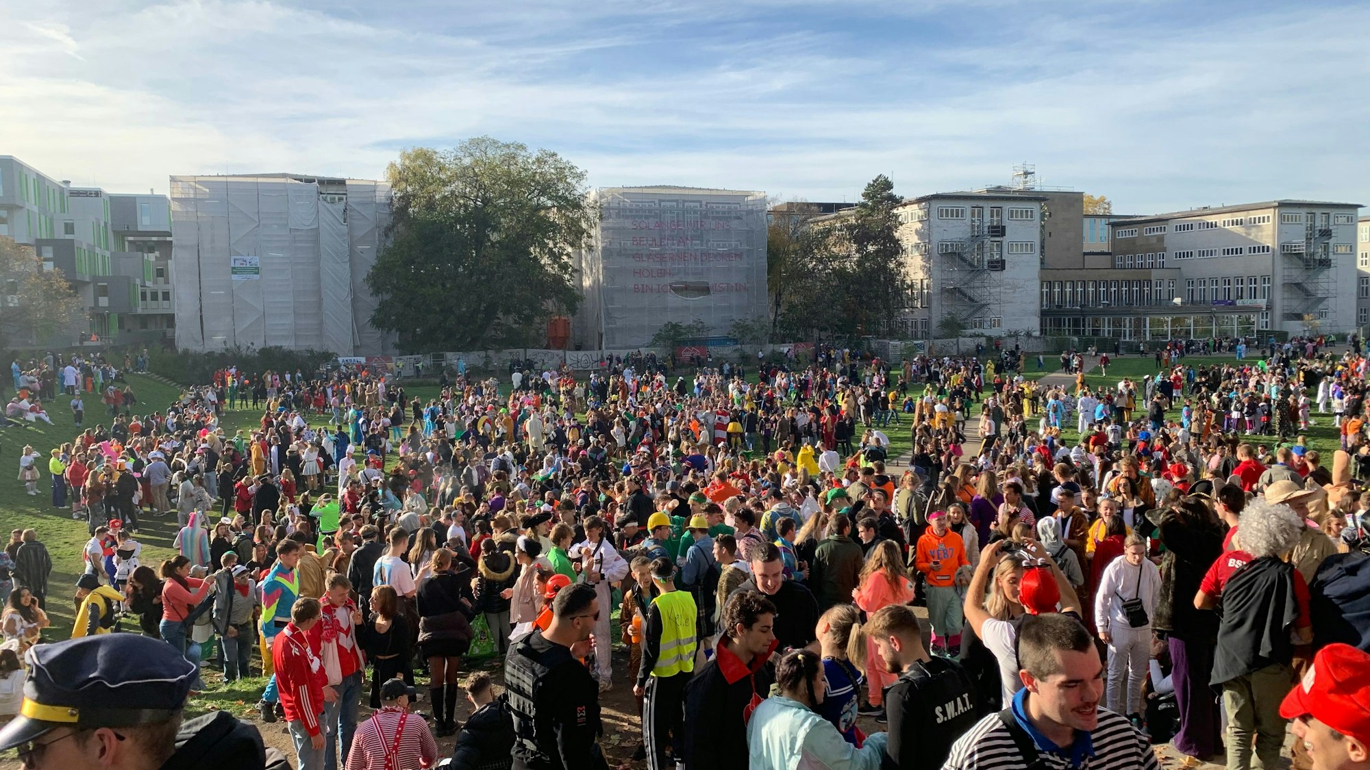Hunderte junge Leute feiern bunt kostümiert am Elften Elften 2022 auf der Uniwiese. Nach den Feierlichkeiten war die Wiese stark verschmutzt. Im Hintergrund ist die Universität zu Köln zu sehen.