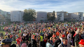 Hunderte junge Leute feiern bunt kostümiert am Elften Elften 2022 auf der Uniwiese. Nach den Feierlichkeiten war die Wiese stark verschmutzt. Im Hintergrund ist die Universität zu Köln zu sehen.