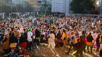 Hunderte Karnevalisten stehen am 11.11. auf einer Wiese vor der Universität.