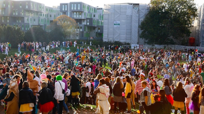 Hunderte Karnevalisten stehen am 11.11. auf einer Wiese vor der Universität.