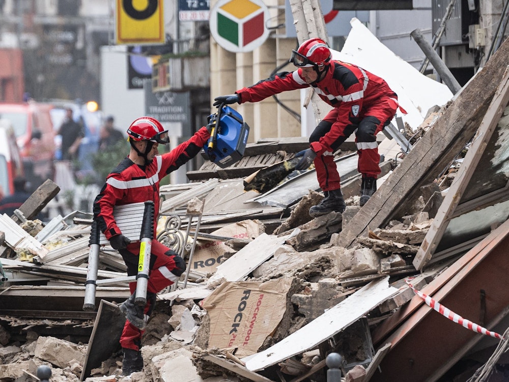 Samstag, 12. November: Zwei Rettungskräfte reichen sich Werkzeuge inmitten der Trümmer eines eingestürzten Gebäudes. Opfer wurden bislang nicht gefunden. Die Häuser waren in der Nacht aufgrund der Meldung eines Anwohners, der nach Hause zurückkehrte, vorsorglich evakuiert worden.
