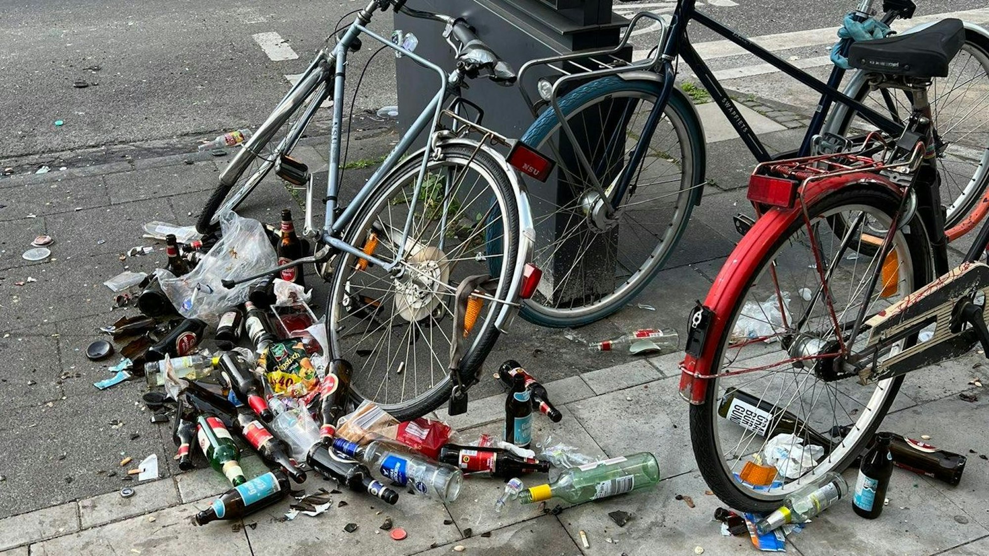 Rund um ein paar abgestellte Fahrräder liegen Dutzende umgestoßene und teilweise zerbrochene Bierflaschen.