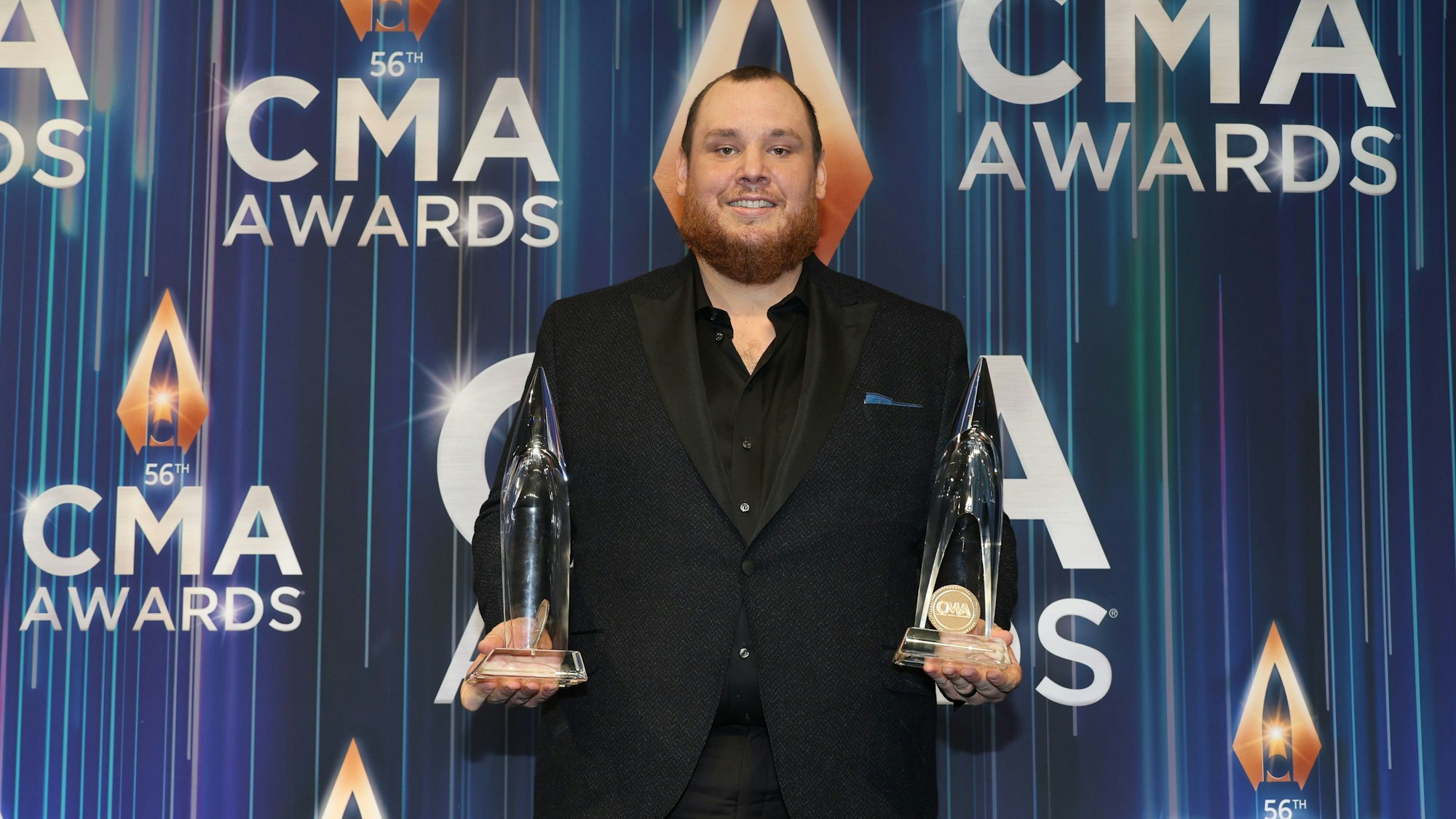 Luke Combs mit den CMA Awards als Entertainer des Jahres und Album des Jahres. Er trägt einen schwarzen Anzug. Beide Trophäen in jeweils der einen Hand.