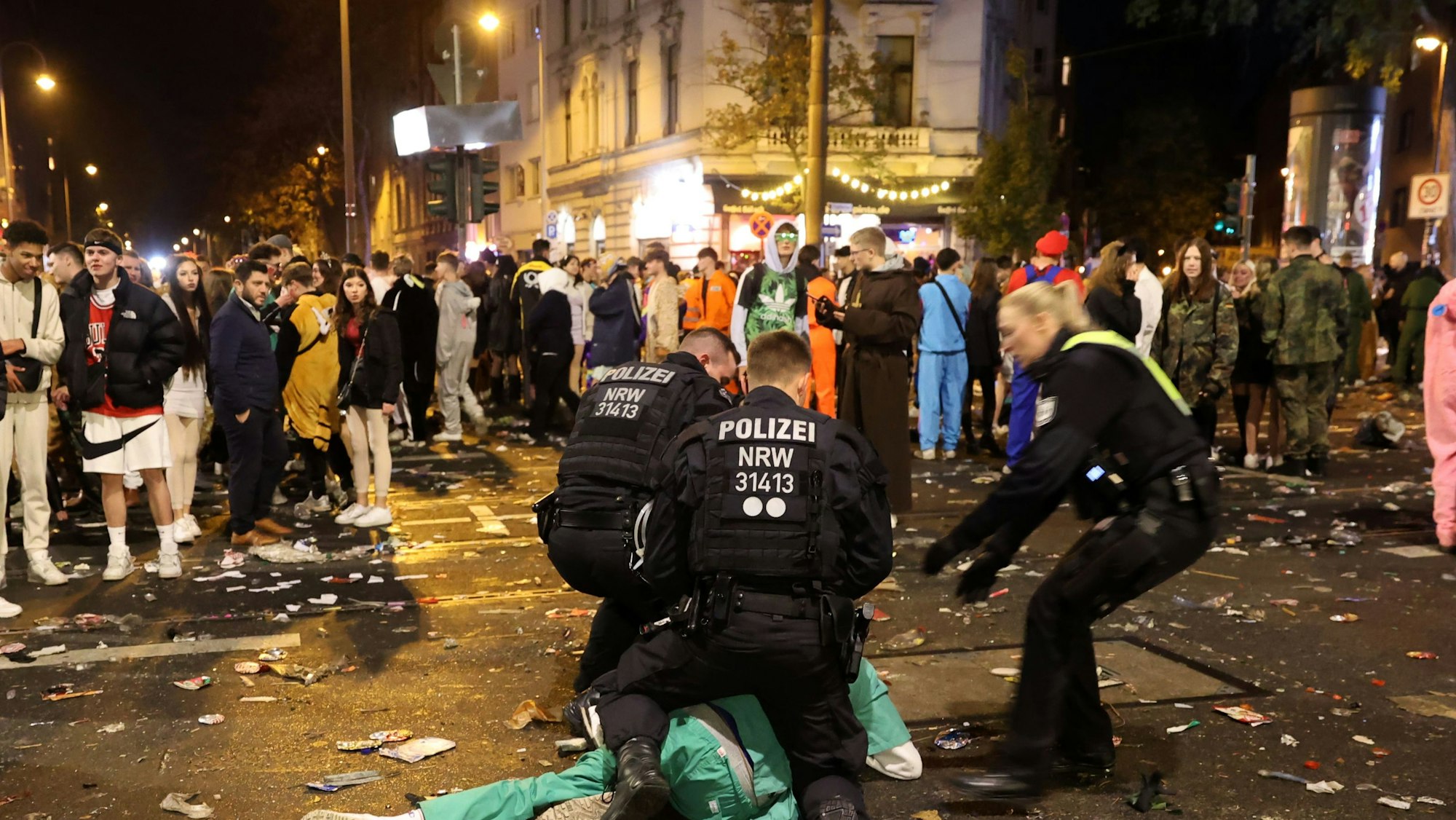 Polizisten beugen sich über einen Karnevalisten in grünem Kostüm. Rundherum stehen Menschentrauben.