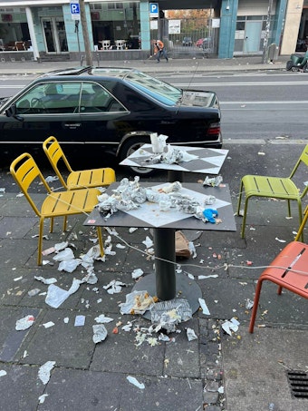 Ein Tisch mit vier Stühlen vor einer Gaststätte an der Aachener Straße ist mit Müll übersät.