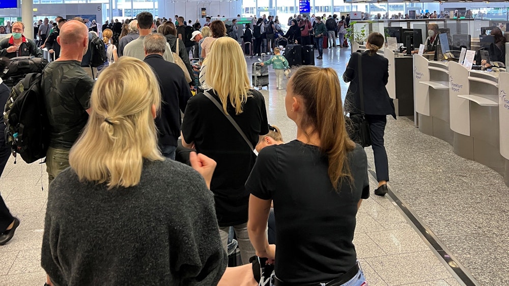 Ferienfluggäste stehen in einer langen Schlange am Frankfurter Flughafen.