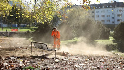 Ein Mitarbeiter der AWB entfernt Müll von den Kölner Uniwiesen
