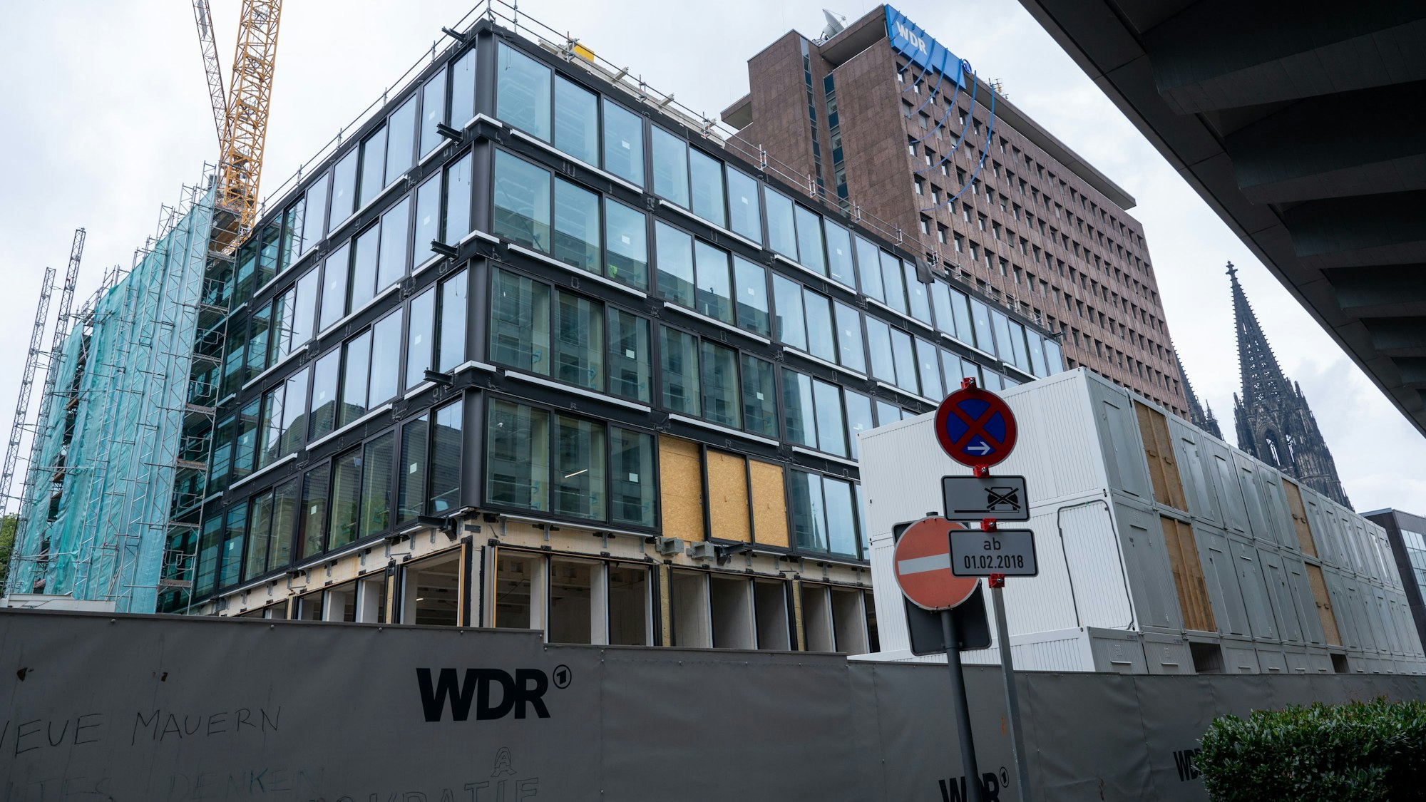 Hinter einem mit den Buchstaben „WDR“ beschriftetem Bauzahn erhebt sich ein mehrgeschossiger Rohbau. In den meisten Etagen sind bereits Fenster eingesetzt.