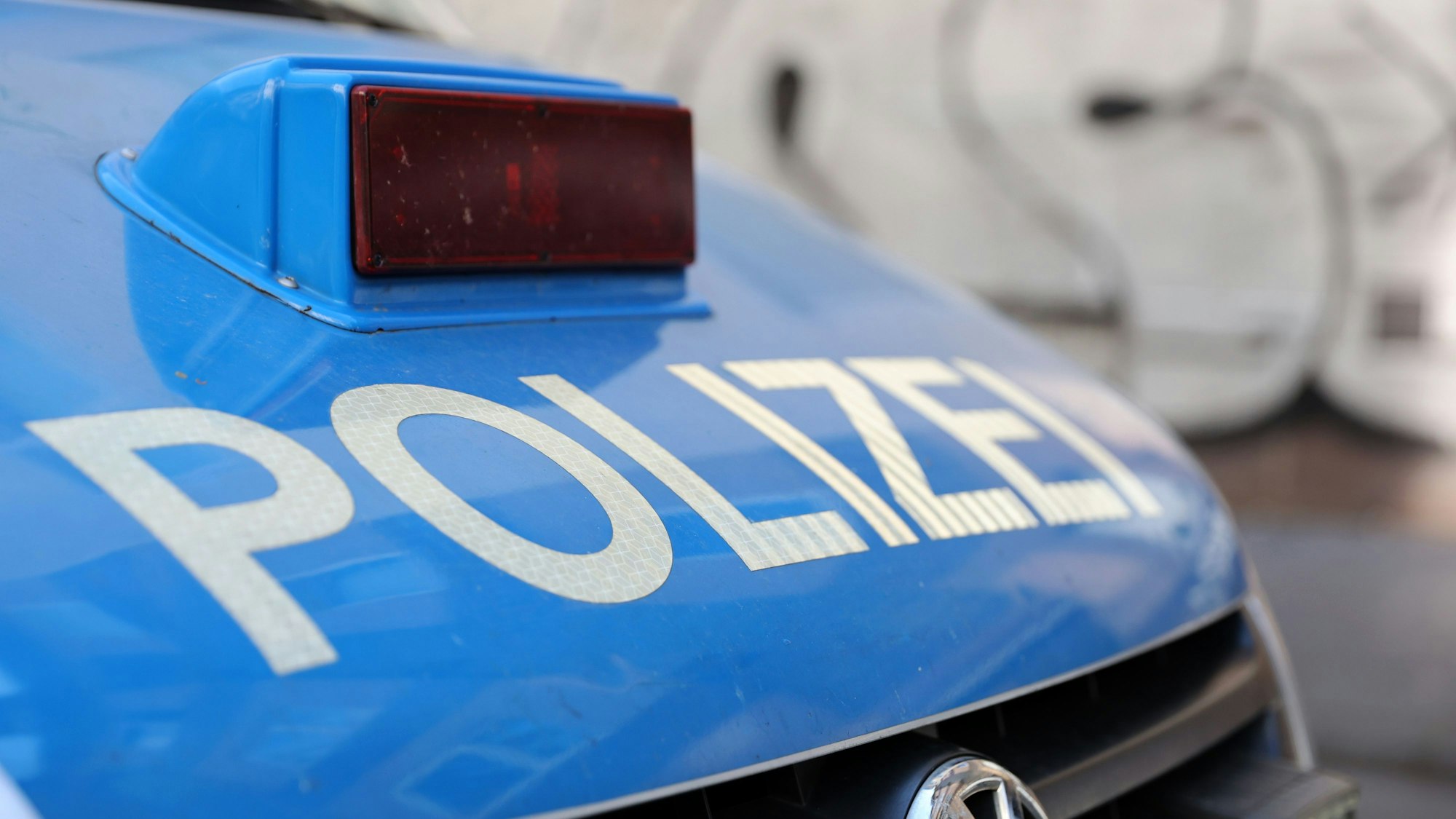 Die Motorhaube eines Polizeiautos mit rot verblendeter Sirene und der weißen Aufschrift „Polizei“.