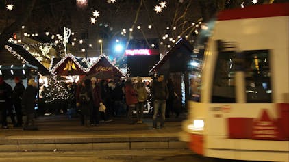 Eine Bahn der KVB hält vor dem weihnachtlich ausgeleuchteten Neumarkt.