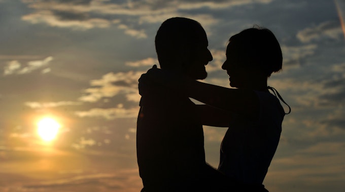 Symbolfoto. Ein junges Paar umarmt sich im Sonnenuntergang.