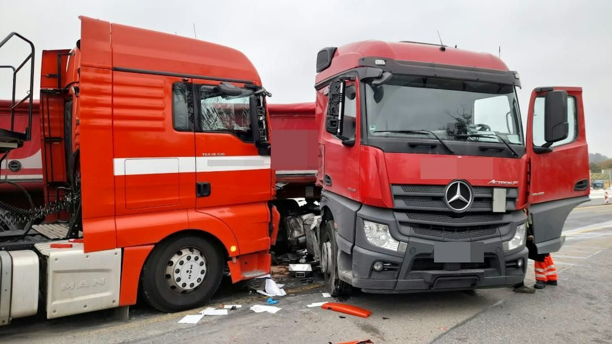 Zwei rote Lkw-Fahrerkabinen stehen beschädigt auf der Autobahn. Auf dem Boden liegen Papiere und abgeplatztes Plastik verteilt.
