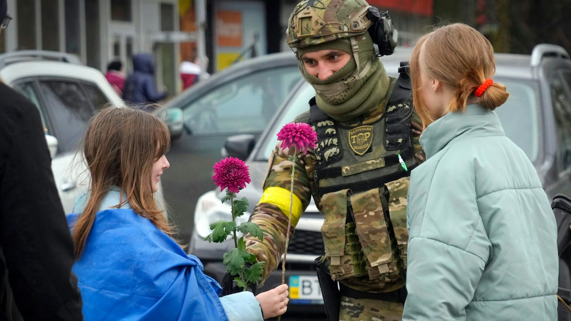 Ein Mädchen, das eine ukrainische Nationalfahne trägt, tauscht mit einem ukrainischen Soldaten in Cherson Blumen aus.