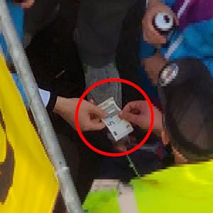 Ein kostümierter Mann drückt einem Ordner gut erkennbar fünf Euro in die Hand.