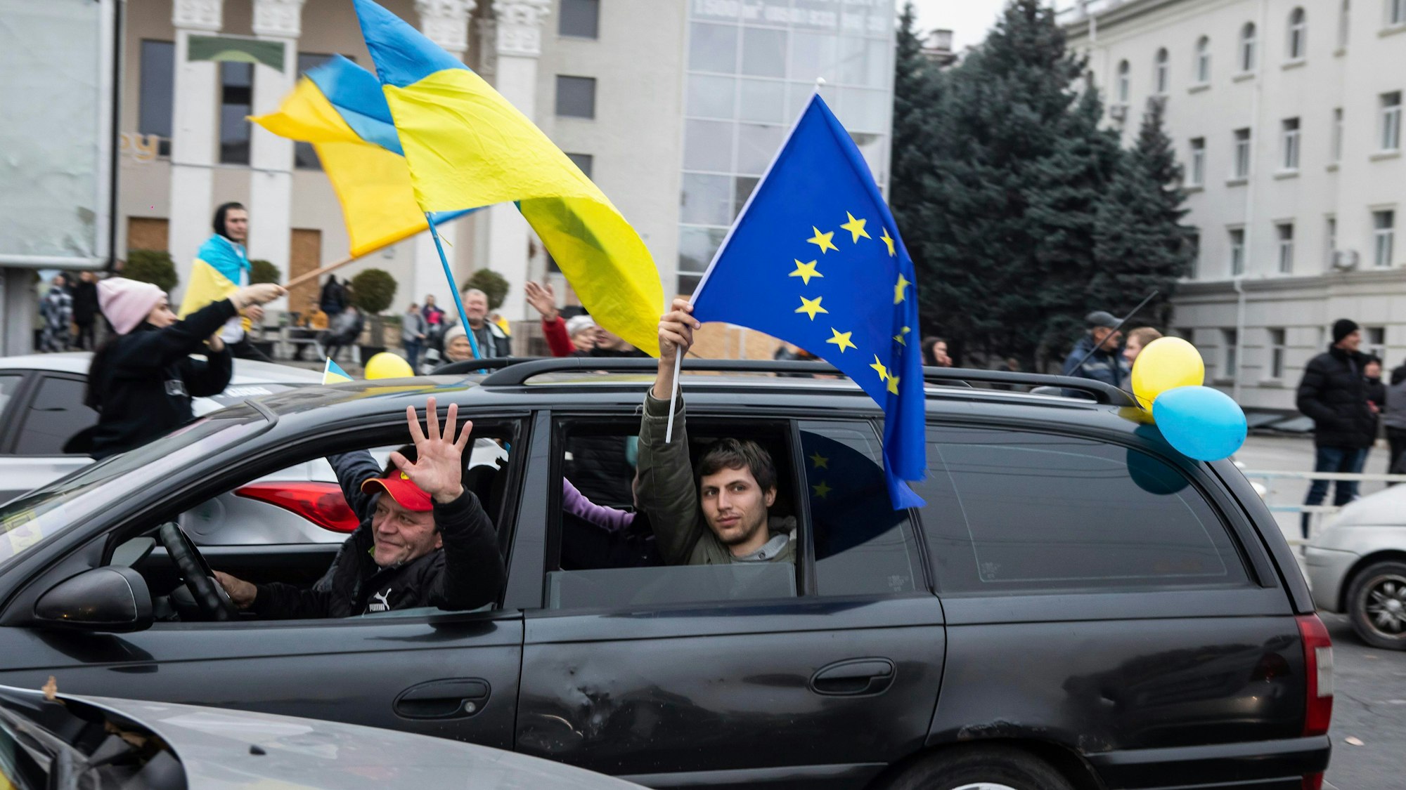 Ukrainer fahren in einem Auto durch das Zentrum von Cherson und halten ukrainische Fahnen aus dem Auto. Auch eine Fahne der EU wird gezeigt.