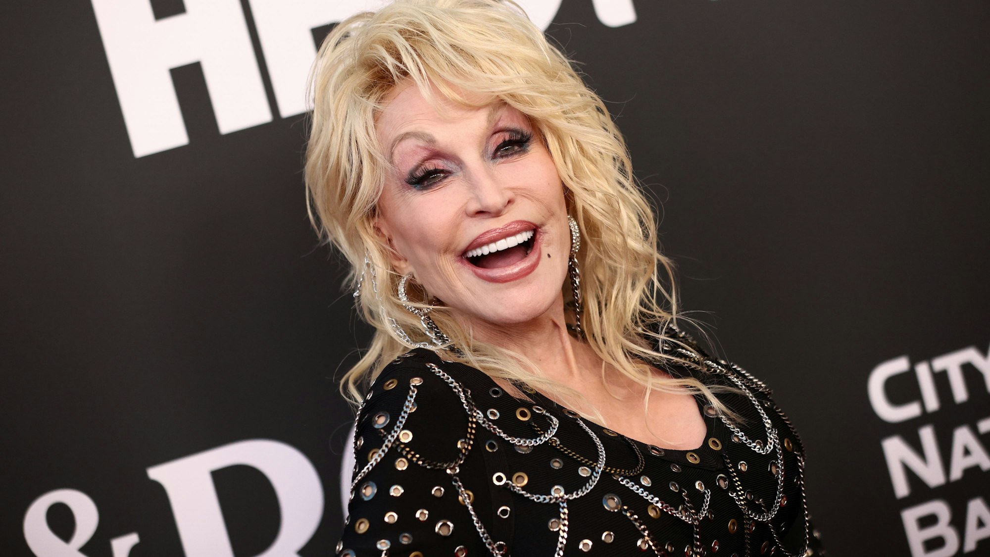 Dolly Parton lacht vor einem HBO-Schild für die Fotografen auf dem roten Teppich.