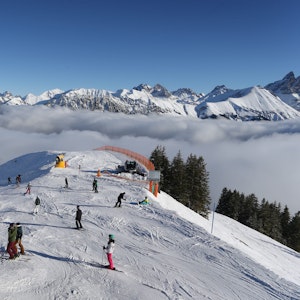 Wintersportlerinnen und Wintersportler fahren auf dem Fellhorn über den Wolken im Sonnenschein.