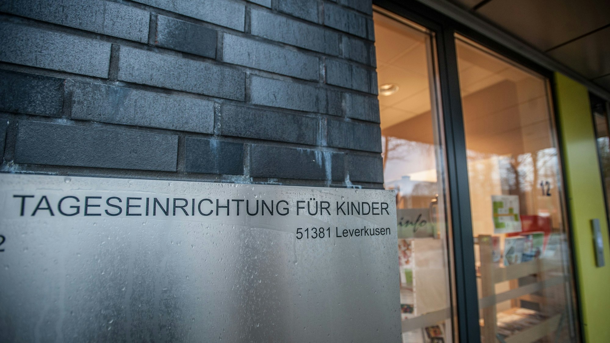 Ein Schild „Tageseinrichtung für Kinder, 51381 Leverkusen“ ist an einer Gebäudewand angebracht.