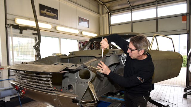 Der alte Ford steht auf einem Wagenheber. Peter Kaufmann arbeitet mit einem Werkzeug in der Hand an der Karosse.