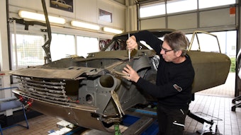 Der alte Ford steht auf einem Wagenheber. Peter Kaufmann arbeitet mit einem Werkzeug in der Hand an der Karosse.