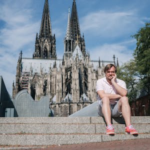 Der Moderator und Autor Nilz Bokelberg sitzt vor dem Kölner Dom.