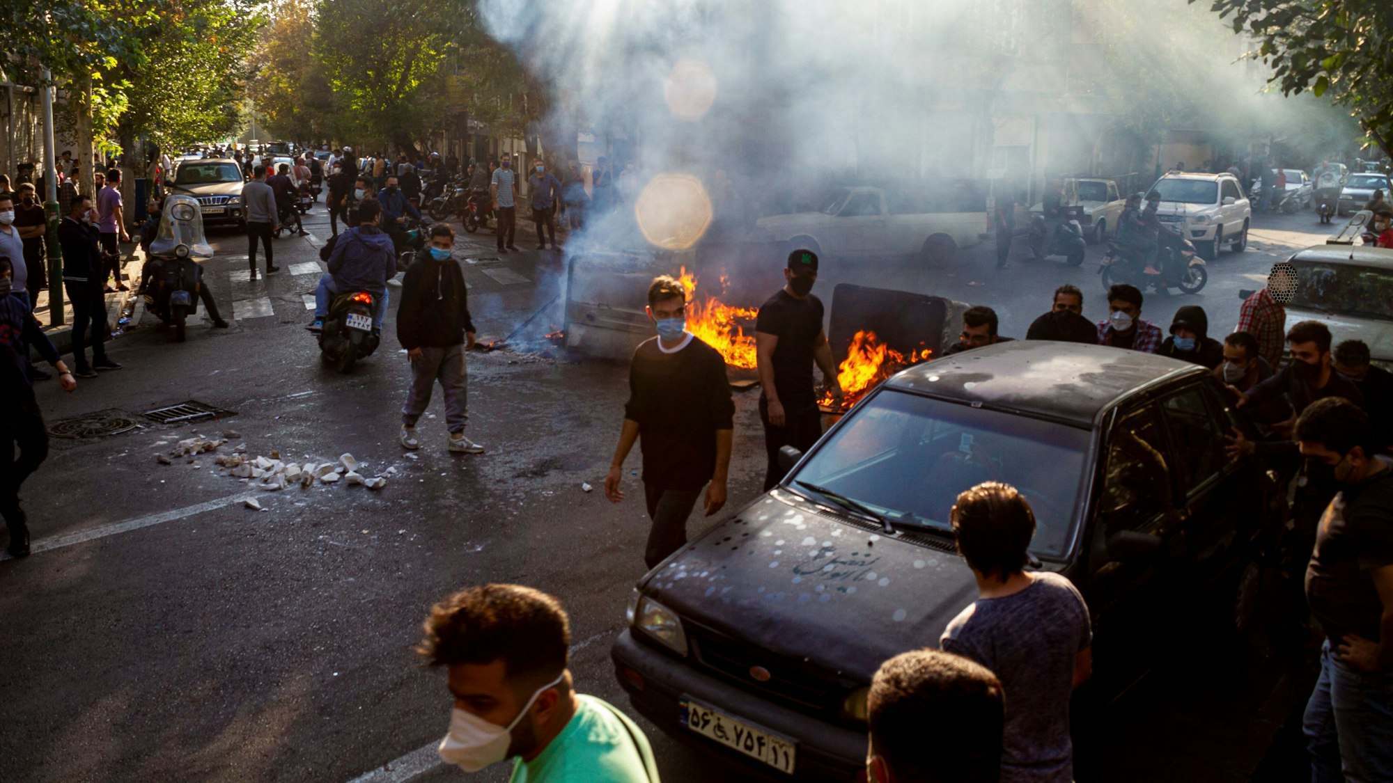 Menschen protestieren in Teheran auf der Straße und haben Barrikaden errichtet. Es brennen Feuer. Viele Demonstranten tragen Gesichtsmasken.