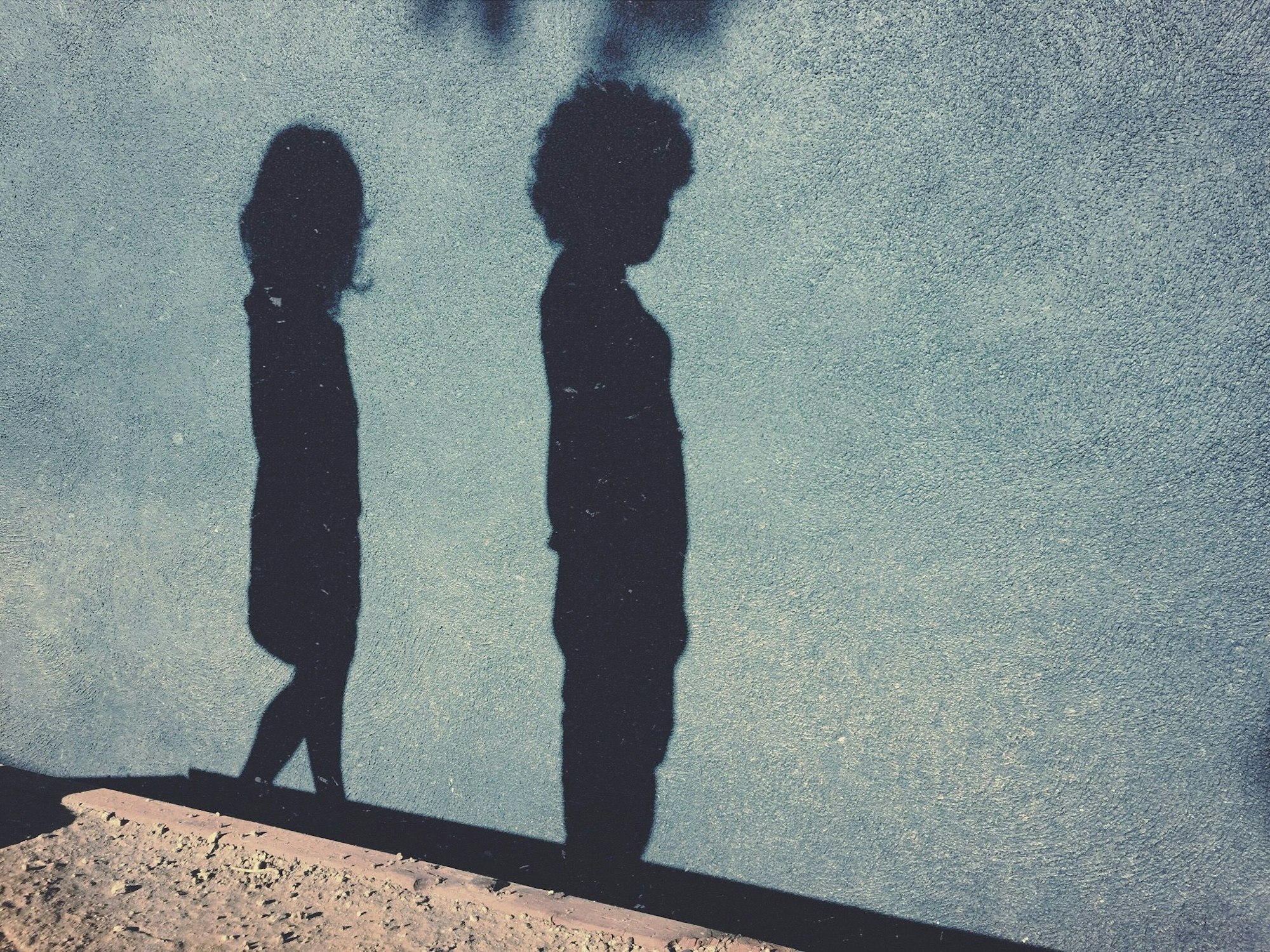 Die Schatten eines Jungend und eines Mädchens sind auf einer blauen Hauswand zu sehen.